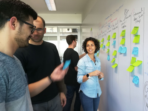 Andreia in the OutSystems office in front of a whiteboard covered in post-its and smiling at a teammate.