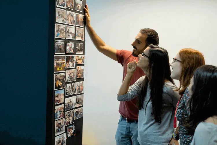 Sara Gonçalves looking at pictures hanging on a wall at OutSystems with two other team members